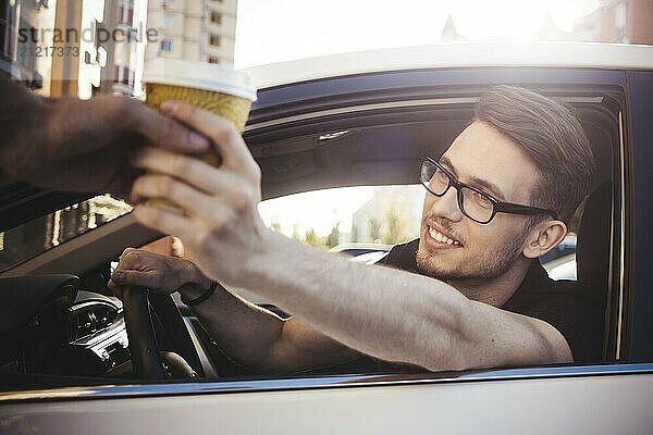 Young smiling man driving car and taking away coffee