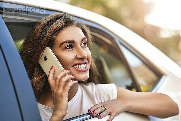 Beautiful woman with phone smiling while sitting on the back seat in the car