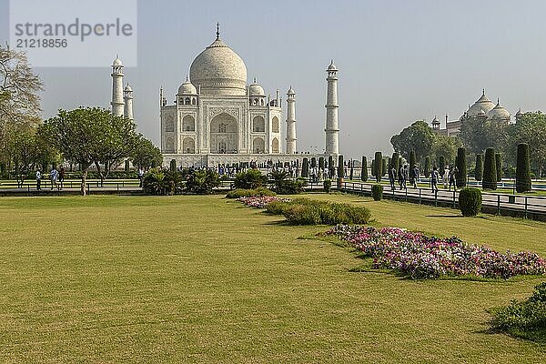 Taj Mahal  das Mausoleum  das Mumtaz Mahal von ihrem Ehemann  dem Mogulkaiser Shah Jahan  errichten ließ. Blick vom Garten  dem Charbagh  mit einer großen Rasenfläche im Vordergrund und einigen blühenden Blumen. Aufgenommen am Morgen eines Tages Mitte April  in der Vormonsunzeit  im Sommer. Weltwunder  UNESCO Weltkulturerbe  berühmtes Wahrzeichen und Touristenattraktion. Agra  Uttar Pradesh  Indien  Asien