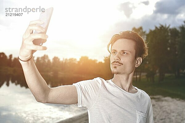 Portrait of Young handsome stylish smiling guy makes selfie against the beach. beautiful nature