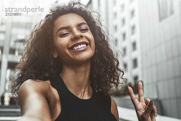 Outdoor portrait beautiful happy afroamerican woman taking selfie photograph smiling laughing with perfect teeth at street