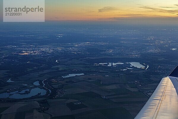 Blick aus einem Flugzeug auf eine weitläufige Landschaft bei Abenddämmerung mit sichtbaren Stadtlichtern  Flug  Luftaufnahme