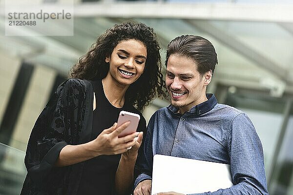 Business man and woman looking at smartphone together on building background in city outdoor feeling happy