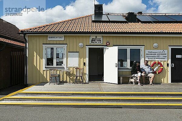 Schweden  30.07.2019: Fassade und zwei ältere Menschen  die vor einem alten Hafenbüro oder hamnkontoret für Grenzkontrollen sitzen  Europa