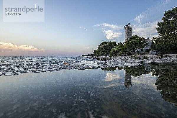 Beautiful sunset in a landscape on a rocky coast with a prominent lighthouse and pine forest. View over the coast to the building  on the Mediterranean Sea  Vir  Dalmatia  Croatia  Adriatic Sea  Europe