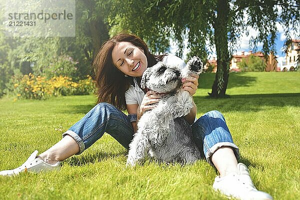 Hübsche erwachsene kaukasische glückliche Frau ruht im Park an einem sonnigen Tag mit ihrem geliebten Hund. Weibliche lag auf dem Gras lächelnd und Blick in die Kamera