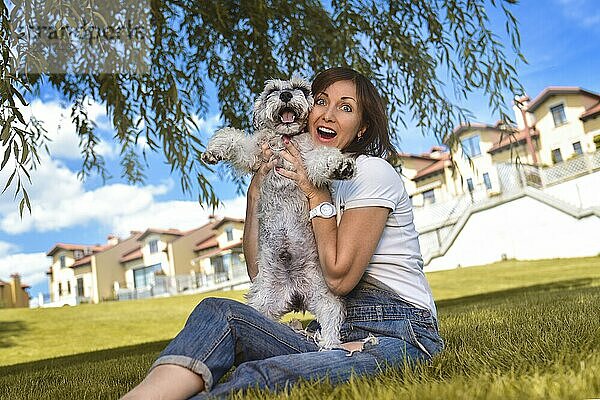 Caucasian joyful woman playing with her beloved dog in the park. The concept of love for animals. best friends. Dog breed Schnauzer