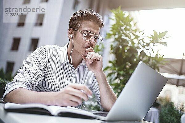 Glücklich gut aussehend Geschäftsmann mischt seine Pause und Arbeit im Freien  Geschäftsmann mit Kopfhörer schreiben einige neue Ideen in Notebook sitzen im Café