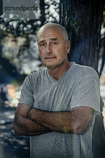 Half portrait  man  50 plus  camera view  bald head  arms crossed  background blurred  edge of forest  Germany  Brandenburg  Storkow  public ground  Europe