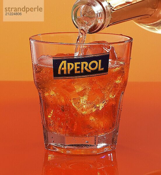 Aperol on ice cube cubes in an aperitif tumbler against an orange background is topped up with soda water