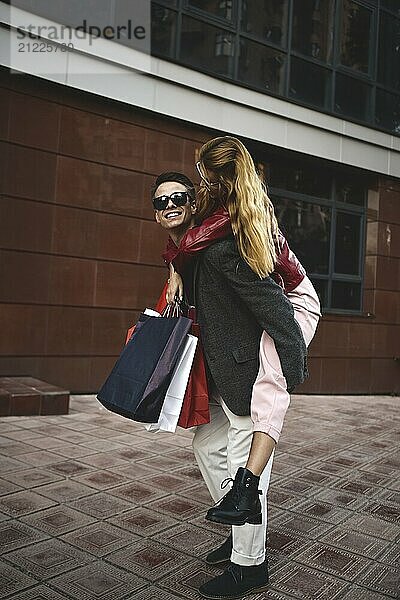 Happy couple shopping together and having fun. Boyfriend carrying his girlfriend on the piggyback