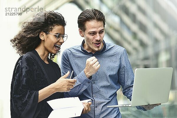 Business man and woman working on laptop together on building background in city outdoor feeling happy