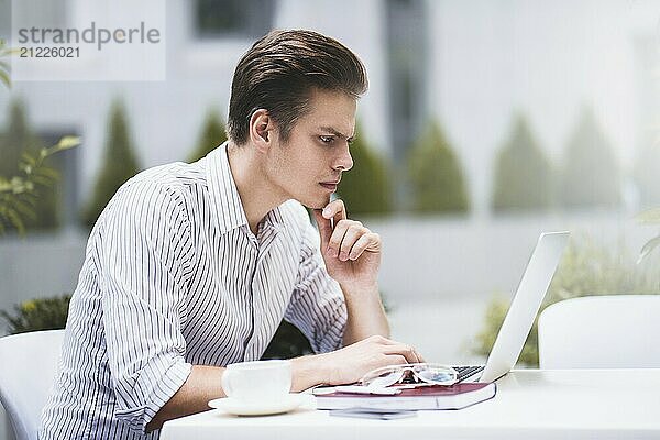 Smart attitude. Positive handsome man using a laptop and sitting in the cafe while surfing the internet