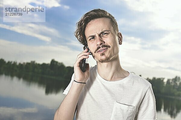 Portrait of angry confused aggressive in bad mood guy irritably speaks on the phone on the background of the lake