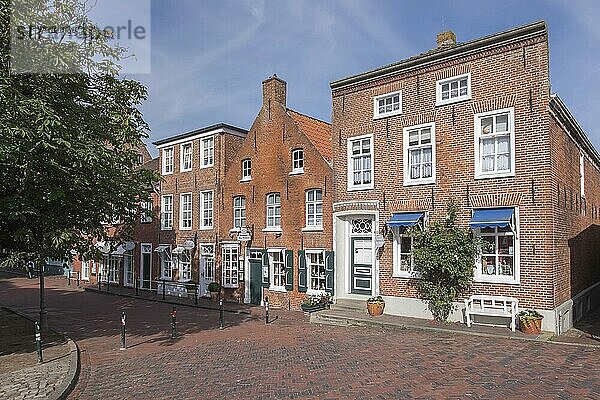 Backsteinhäuser entlang einer gepflasterten Straße bei sonnigem Wetter  historischer Stadtkern mit Bäumen und Fenstern  Atmosphäre heiter  Fischerort Greetsiel  Krummhörn  Ostfriesland  Niedersachsen  Deutschland  Europa