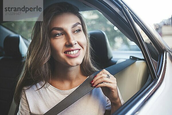 Beautiful woman with phone smiling while sitting on the back seat in the car