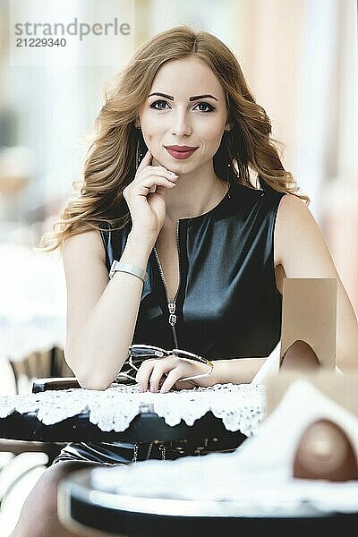 Attractive young caucasian woman sitting in street cafe  waiting for someone  having coffee  having great time. She wearing black stylish dress