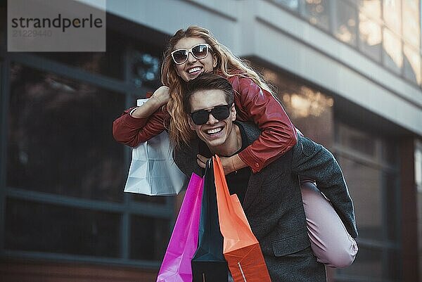 Happy couple shopping together and having fun. Boyfriend carrying his girlfriend on the piggyback