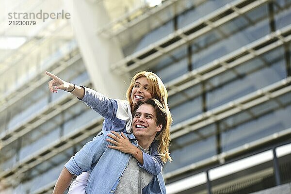 Man giving his pretty girlfriend a piggy back at street smiling at each other on a sunny day