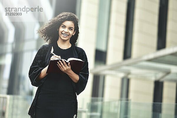 Charming Afro American beautiful happy female  making notes in notepad while walking outdoors on a city street. Education and business concept with space for text