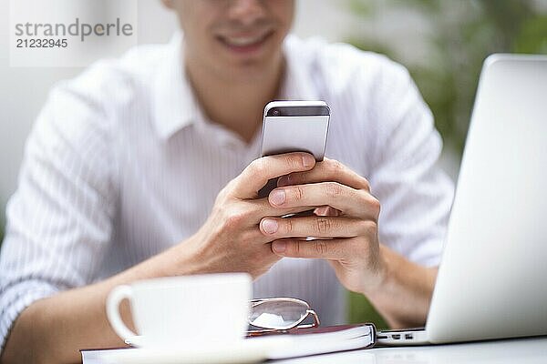 Businessman in white shirt using mobile smart phone and working or browsing internet on laptop computer. Close up photo