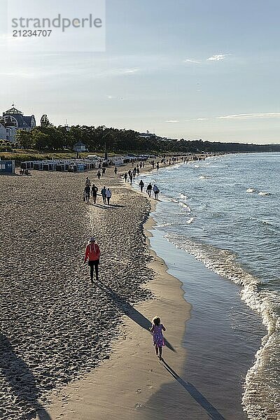 Menschen genießen einen Spaziergang am sandigen Strand entlang der ruhigen Meeresküste  Rügen  Binz