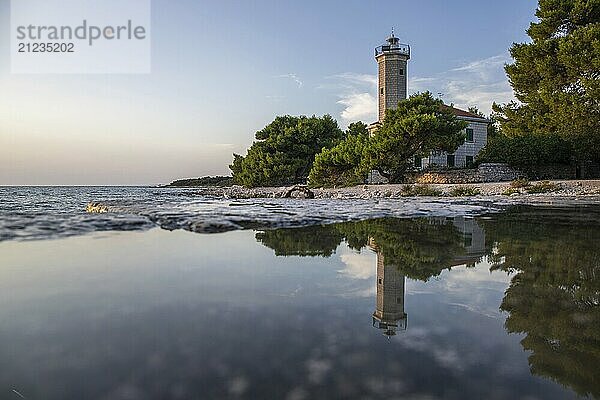 Beautiful sunset in a landscape on a rocky coast with a prominent lighthouse and pine forest. View over the coast to the building  on the Mediterranean Sea  Vir  Dalmatia  Croatia  Adriatic Sea  Europe