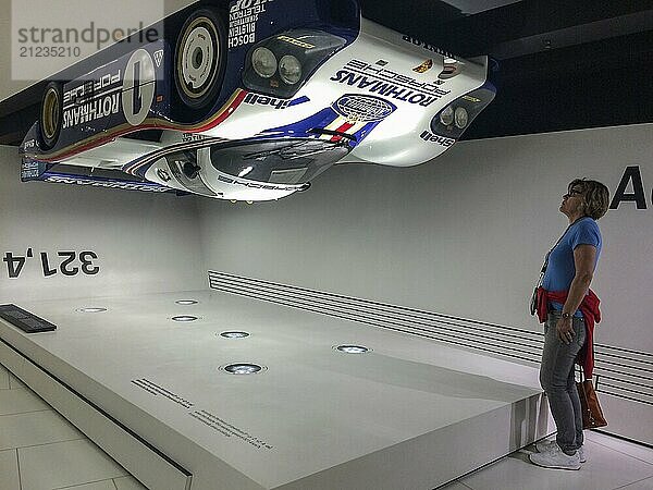 Visitor to the museum looks upwards at a Porsche 956 racing car hanging upside down under the ceiling of the museum as an example of high contact pressure at 321.4 kilometres per hour  Porsche Museum  Stuttgart  Baden-Württemberg  Germany  Europe