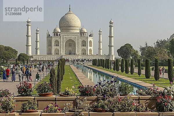 Taj Mahal  the mausoleum built for Mumtaz Mahal by her husband  the Mughal emperor  Shah Jahan. A distant  classic view  with some flowers in the foreground  the water channel reflecting the building  and some colourfully dressed visitors. Photographed in the morning of a mid-April day  the pre-monsoon summer season. Wonder of the World  a UNESCO World Heritage Site  famous landmark and tourist attraction. Agra  Uttar Pradesh  India  Asia