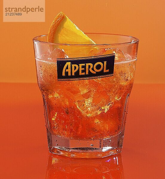 Aperol on ice cube cubes with half an orange slice in an aperitif tumbler against an orange background