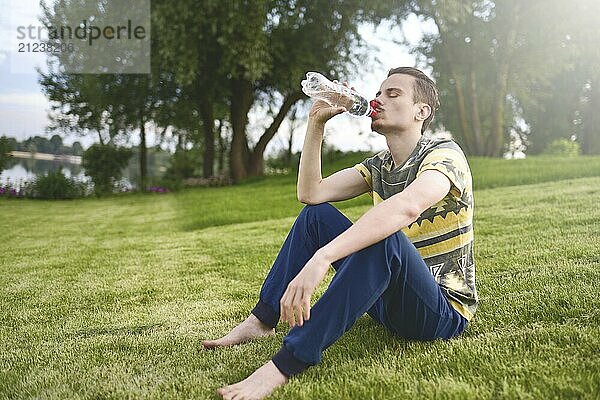 Young man sitting on the garden and drinking water after running