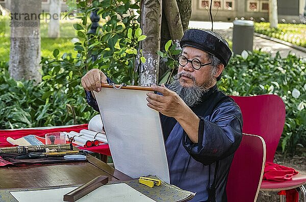 HANOI  VIETNAM  14. NOVEMBER: Alter vietnamesischer Mann in Nationaltracht schreibt Hieroglyphen auf altem Papier auf der Straße am 13. November 2016 in Hanoi  Vietnam  Asien