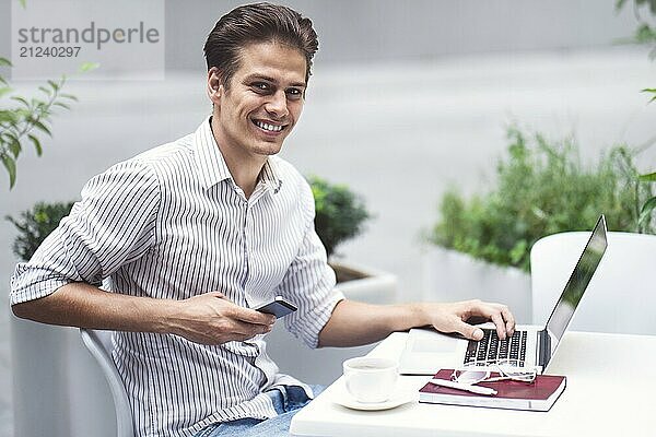 Smart attitude. Positive handsome man using a laptop and sitting in the cafe while surfing the internet