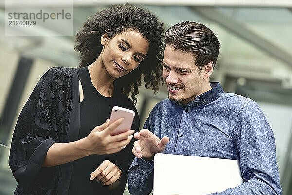 Business man and woman looking at smartphone together on building background in city outdoor feeling happy