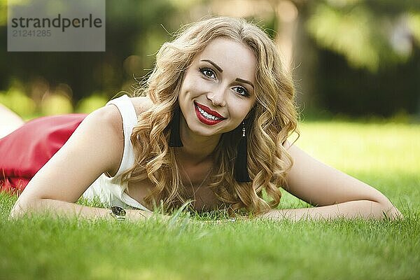 Top view of attractive female model lying on green grass in park and looking at camera during time for taking rest  portrait of Caucasian woman with blond hair spending day at nature.summer time