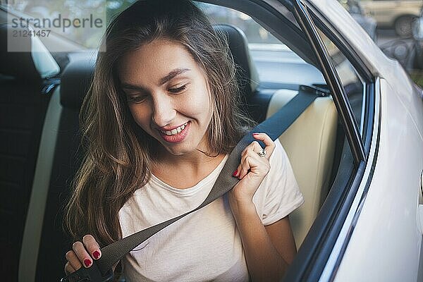 Beautiful woman with phone smiling while sitting on the back seat in the car