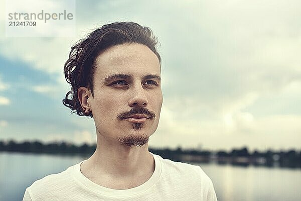 Portrait of Young Man Enjoys a beautiful view and looks into the distance near a lake and forest  summer  spring. nature