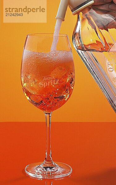 Aperol Spritz against an orange background is topped up with soda water