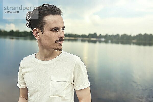 Porträt eines jungen Mannes Genießt eine schöne Aussicht und schaut in die Ferne in der Nähe eines Sees und Waldes  Sommer  Frühling. Natur