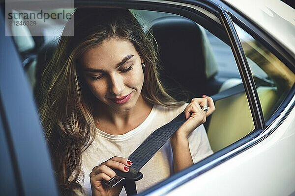 Beautiful woman with phone smiling while sitting on the back seat in the car