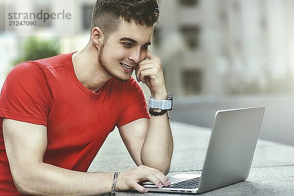 Young attractive guy who is smiling looking at his laptop screen  Young man using laptop