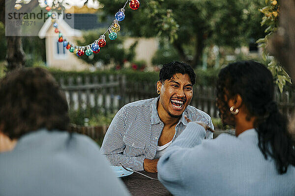 Cheerful young man enjoying while talking to female friend in back yard at dinner party