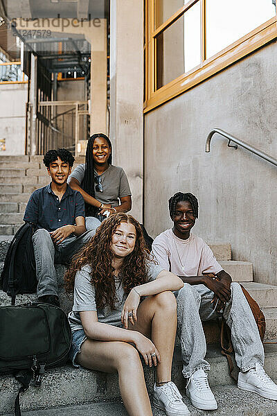 Portrait of multiracial male and female students sitting on stairs of junior high school