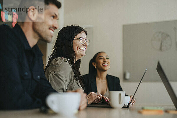 Happy businesswoman with eyeglasses discussing with coworkers in meeting room