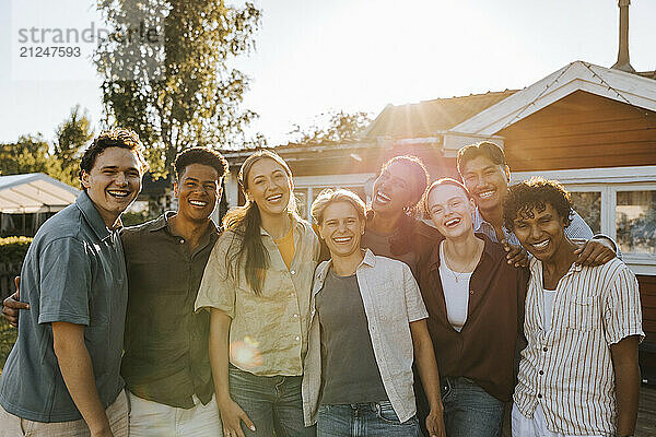 Portrait of happy multiracial group of male and female friends standing in back yard at dinner party