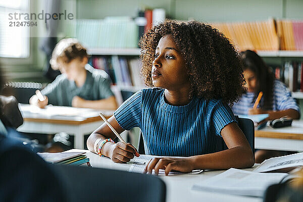 Thoughtful curly hair girl sitting near desk in classroom at elementary school