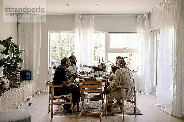 Happy multigenerational family having lunch while sitting together at dining table in home