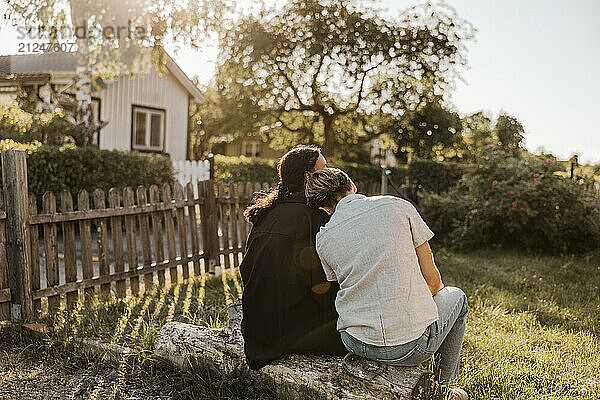 Rear view of young woman sitting with head on shoulder of female friend in back yard