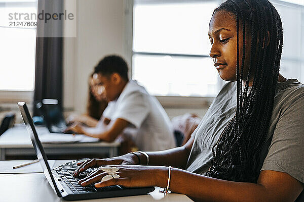 Teenage girl with braided hair doing e-learning in classroom at junior high school