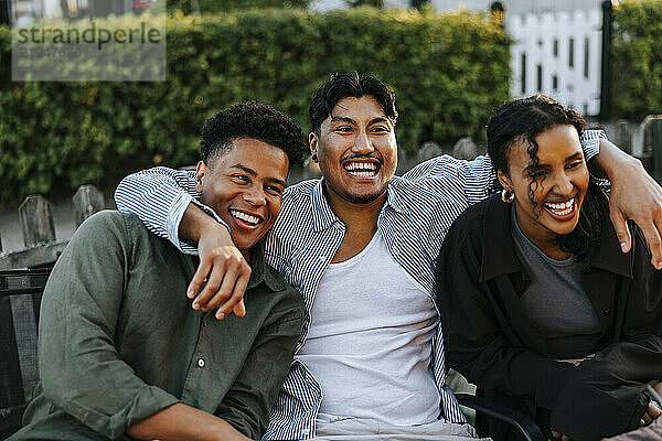 Happy young man with arm around male and female friend enjoying in back yard at social party